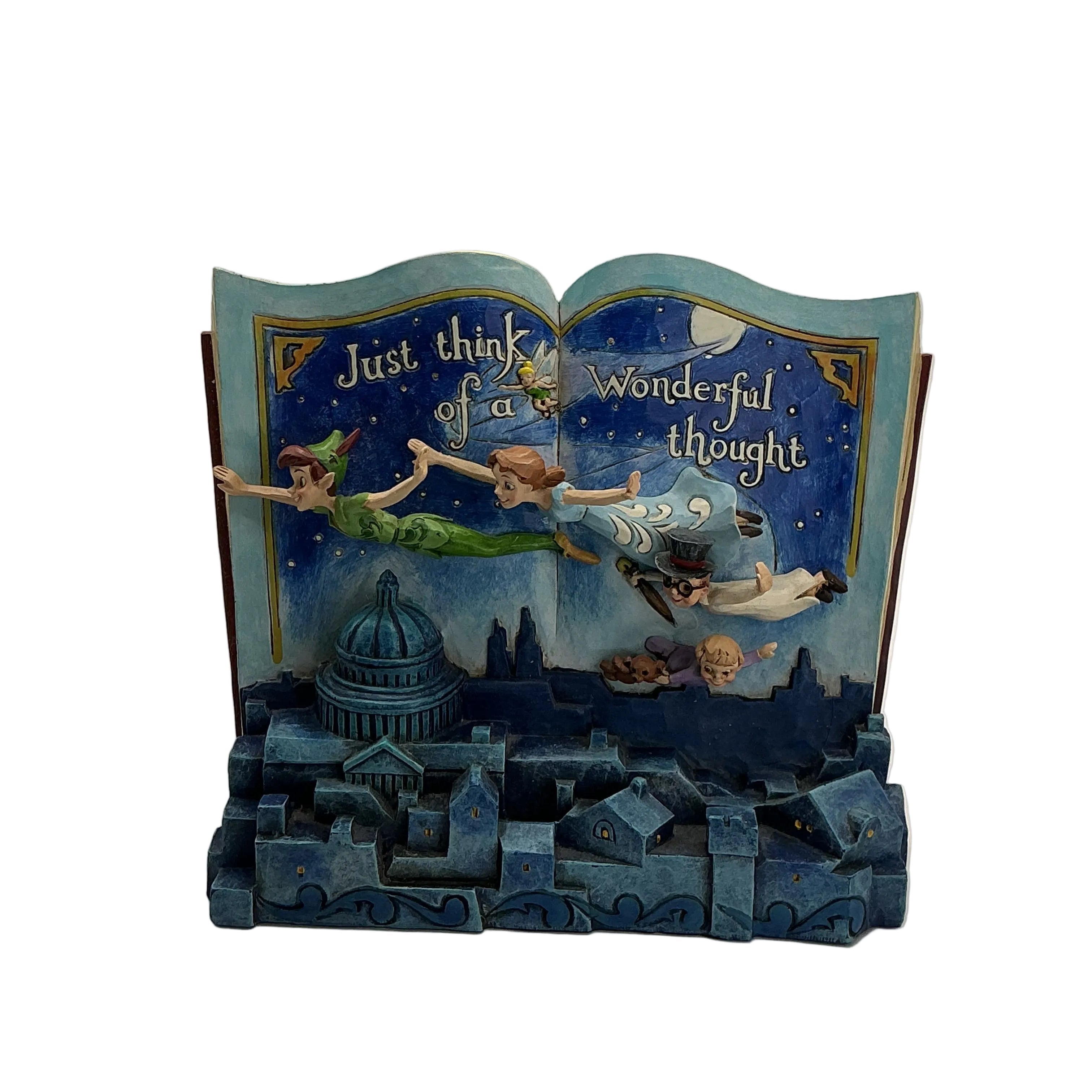 A decorative book-shaped figurine or bookend featuring Peter Pan and Tinker Bell flying above a blue cityscape, with the text 'Just think of us' and 'Wonderful thought' on the open pages, photographed against a plain light gray studio background.